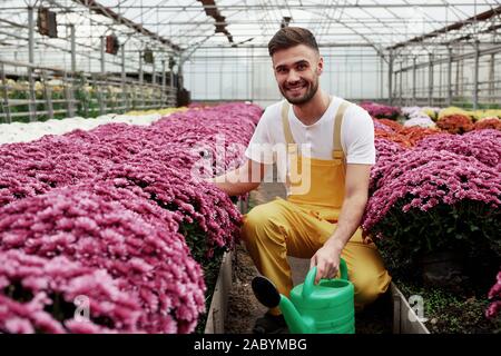 Liebe zur Natur. Foto von schönen jungen Kerl im Gewächshaus die Pflege von rosa gefärbten Blüten Stockfoto