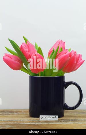 Dank je wel (Danke in Niederländisch) Karte mit Becher voll der Niederländischen rosa Tulpen auf Holz- Oberfläche Stockfoto