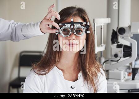 Sie Korrekturen an Gerät. Mädchen trägt eine Brille in Augenklinik und lächelnd im Hintergrund von medizinischen Geräten Stockfoto
