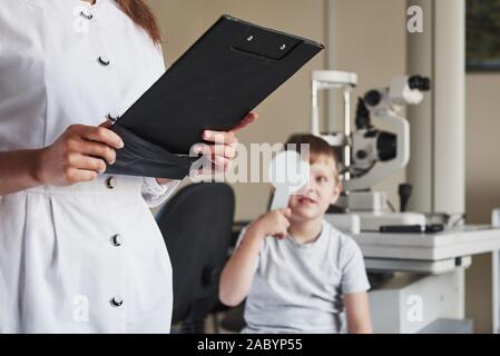 Ständigen und Schreiben. Welche die Prüfung in den Augenarzt Büro mit Kind. Arzt Hinweise Daten Stockfoto