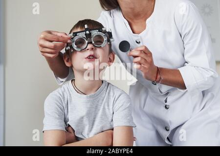 Kaum konzentrieren. Arzt tuning Der phoroptor an Sehschärfe des kleinen Jungen bestimmen Stockfoto