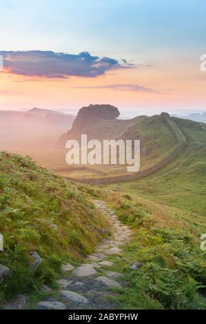 Northumberland National Park. Morgendämmerung Nebel vom Pfad in der Nähe von Cuddy Craig auf Hadrian's Wall auf der Suche nach Osten in Richtung Housesteads Craig und die aufgehende Sonne. Stockfoto