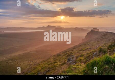 Northumberland National Park. Morgendämmerung Nebel vom Pfad in der Nähe von Cuddy Craig auf Hadrian's Wall auf der Suche nach Osten in Richtung Housesteads Craig und die aufgehende Sonne. Stockfoto