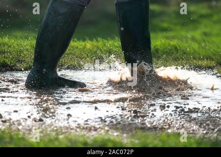 Person in grünen Gummistiefeln wandern in einer großen nassen schlammigen Pfützen im frühen Morgenlicht kopieren Platz an der Basis der Bild Stockfoto