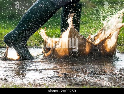 Grüne Gummistiefel planschen in einem großen nassen schlammigen Pfützen im frühen Morgenlicht kopieren Platz an der Seite des Bildes Stockfoto
