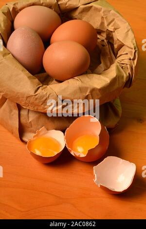 Ein Papier shopper voller Frische Eier anda gebrochen Ei auf dem hölzernen Tisch. Stockfoto