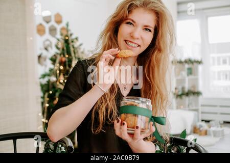Glückliche junge Frau, die essen Weihnachtsplätzchen in Küche und lächelnd Stockfoto