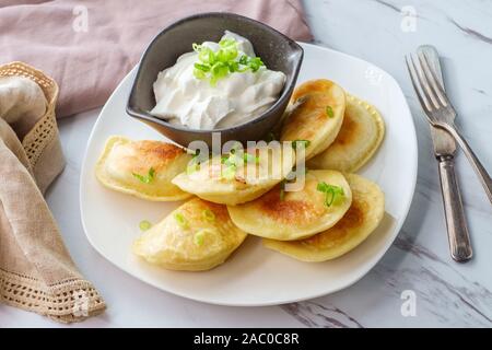 Köstliche authentische polnische Piroggen mit gehackten Frühlingszwiebeln und Sauerrahm Stockfoto