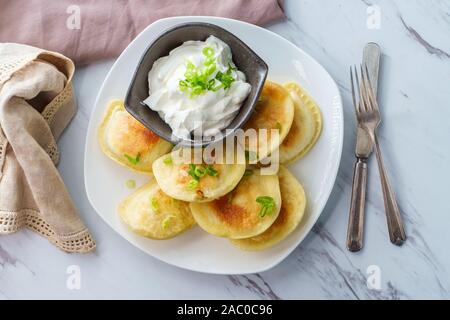 Köstliche authentische polnische Piroggen mit gehackten Frühlingszwiebeln und Sauerrahm Stockfoto