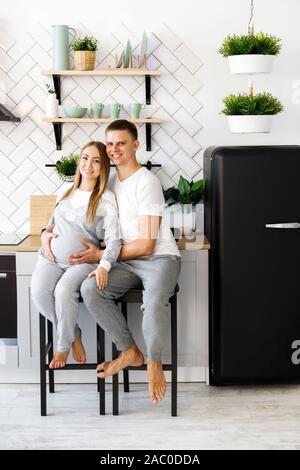 Junges Paar - Mann und Frau, die ein Baby erwarten, verbringen viel Zeit in der Küche. Stockfoto