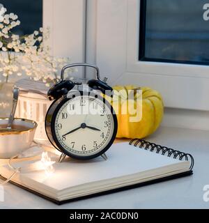 Gypsophila Strauß auf das Fenster in ein Glas Vase in der Abenddämmerung. Tasse Tee mit Zitrone. Die Uhr zeigt halb drei. Stockfoto
