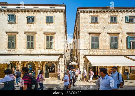 Touristen zu Fuß die Hauptstraße oder Stradun, wie Sie eine schmale Treppe an der Wand, das in der ummauerten Stadt Dubrovnik Kroatien übergeben. Stockfoto