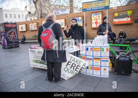 Stehende Männer reden am Stall, in dem der Quran kostenlos angeboten wird, am Freien Quaran Islam Religion stand stand in Leicester Square London Stockfoto