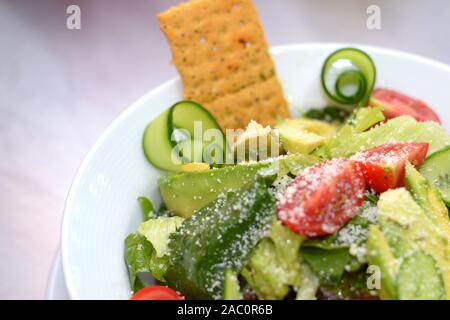 Avocado Salat, frische Scheiben Avocado mit Spiralised Gurke, Tomate und frische grüne Blätter, mit Parmesan bestreut. In einer Runde weiße Schüssel Stockfoto