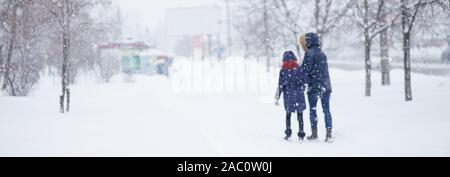 Von einem Mann entlang eine verschneite Straße. Starker Schneefall in der Stadt. Verschwommenes Bild von Mutter und dauther. Web Promo Banner Hintergrund für Ad Stockfoto