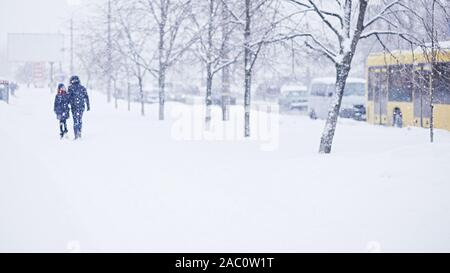 Von einem Mann entlang eine verschneite Straße. Starker Schneefall in der Stadt. Verschwommenes Bild von Mutter und dauther. Web Promo Banner Hintergrund für Ad Stockfoto