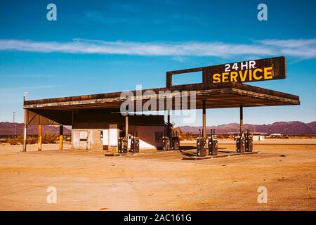 Verlassene Tankstelle mit Schild "24-Stunden-Service" mit Vintage Look in der Wüste gegen den blauen Himmel und Wolken,, Stockfoto