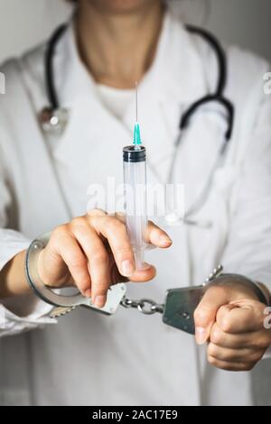 Nahaufnahme von einem Arzt in Handschellen mit einer Spritze in der Hand. Das Konzept zur Einführung der verbotenen Drogen zu den Patienten Stockfoto