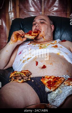 Fat couch potato Essen einer riesigen Hamburger und Fernsehen. Grelle Beleuchtung aus dem Fernsehen beleuchtet die dunklen Zimmer. Stockfoto