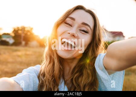 Foto von Angeregten kaukasische Frau unter selfie Foto und Lachen beim Gehen in die Landschaft während der sonnigen Tag Stockfoto