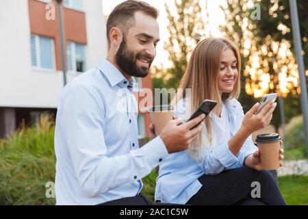 Bild einer jungen gerne Kollegen Mann und Frau Geschäftsleute draußen auf der Straße mit Handys sitzen. Stockfoto