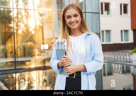Foto eines Jungen glücklich lächelnde Frau, die draußen auf der Straße in der Nähe von Business Center holding Zwischenablage. Stockfoto