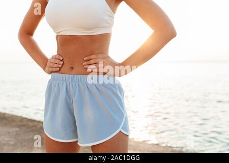 Zugeschnittenes Bild von Fitness kaukasische Frau in Sportswear stehend mit Waffen an der Hüfte, während Sie trainieren von Meer in Morgen Stockfoto