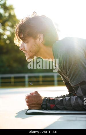 Foto Nahaufnahme des jungen kaukasischen Mann in Sportkleidung, übung auf der Matte, während sie auf dem Spielplatz im Freien arbeiten Stockfoto