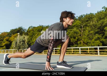 Foto von athletischen konzentriert man in Sportkleidung Übungen auf der Matte, während sie auf dem Spielplatz im Freien arbeiten Stockfoto