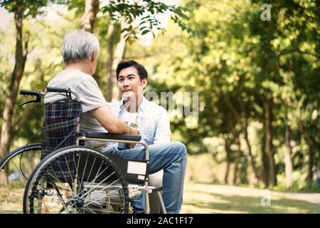 Asiatische Sohn zu reden und tröstend Rollstuhl Vater Stockfoto