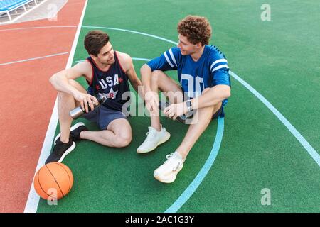 Zwei attarctive passen Männer Basketball Spieler sitzen auf einem Sportplatz, im Gespräch Stockfoto