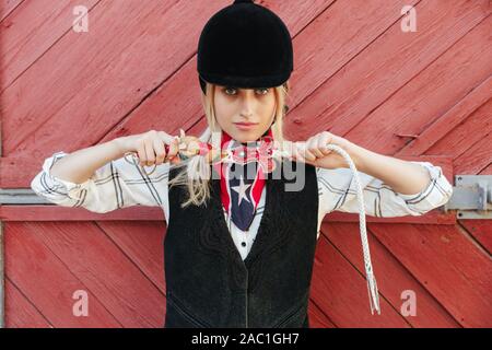 Lächelnde blonde Mädchen Jockey am Stall, Holding pferdepeitsche Stockfoto