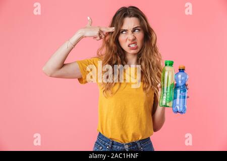 Foto der nervösen kaukasische Frau in Basic t-shirt Holding Plastikflaschen und gun Geste über rosa Hintergrund isoliert Stockfoto