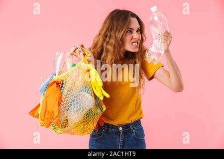 Foto der jungen wütenden Frau mit Tasche mit Kunststoffabfällen und Flasche Kamera über rosa Hintergrund isoliert Stockfoto