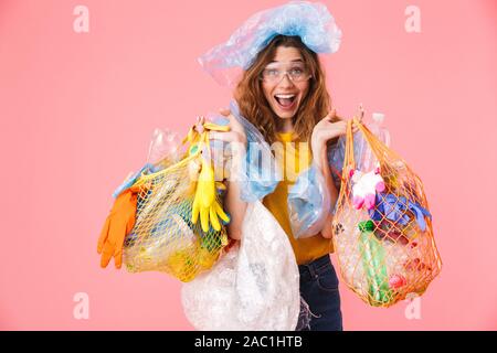 Foto der jungen Frau holding Taschen mit Kunststoffabfällen und lächelnd über rosa Hintergrund isoliert Stockfoto