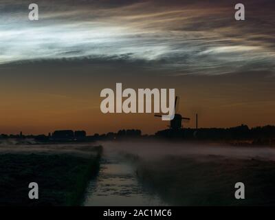 Windmühle, Nebel Banken und hell leuchtenden Nachtwolken (NLC) über die niederländische Landschaft während Ein Sommernachtstraum Stockfoto