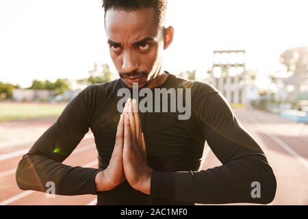 Bild des athletischen african american man Handflächen Holding am Sportplatz im Freien Stockfoto