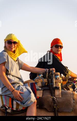 Douz, Tunesien - 8 September, 2014: Zwei lächelnde junge Frauen auf einem Kamel reiten durch die Wüste Sahara. Es wird häufig von Touristen getan Stockfoto