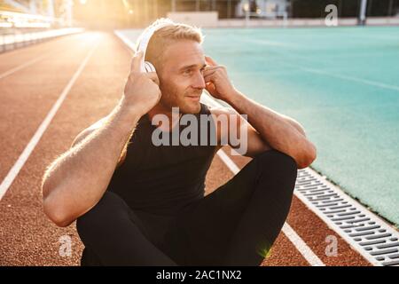 Bild der muskulöse Sportler Musik hören mit Kopfhörern beim Training im Stadion im Freien Stockfoto