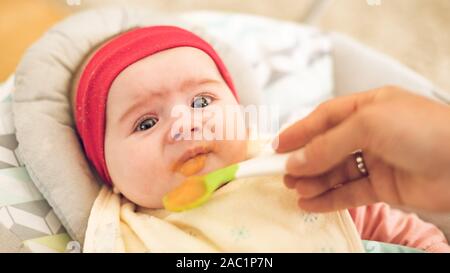 Mutter Fütterung hungrigen fünf Monate alten lustig Baby mit fester Nahrung. Stockfoto