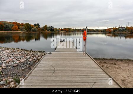 Freunde sitzen auf einem Pier am Töölönlahti Bucht an einem dunkel Herbst Tag in Helsinki, Finnland Stockfoto