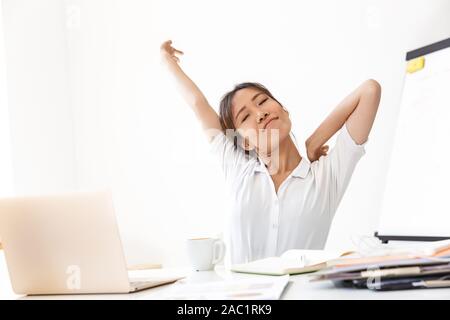Attraktive junge asiatische Geschäftsfrau Arbeiten am Schreibtisch im Büro sitzen, Stretching Hände Stockfoto