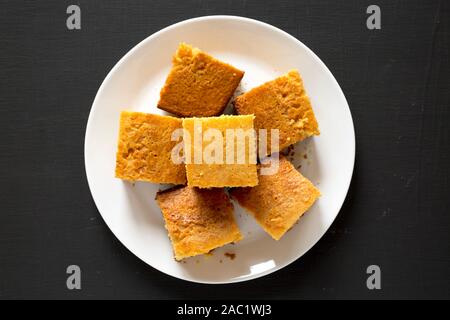 Hausgemachte geschnitten Cornbread bereit zu Essen auf einer weißen Platte auf eine schwarze Fläche, Ansicht von oben. Flach, Overhead, von oben. Close-up. Stockfoto