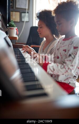 Weihnachten, Winter Urlaub, Silvester Party und Familie Konzept. Junge Mutter mit Kind spielen Musik am Piano. Stockfoto