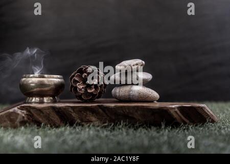 Pyramide von zen Steine, Tannenzapfen und brennende Kerze auf alten Holz- Hintergrund, Meditation Konzept, dunkel getönt Stil. Zen Hintergrund Stockfoto