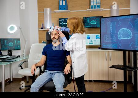 Arzt, der Gehirnwellen setzt Scangerät auf einer männlichen Patienten. Klinische Studie Stockfoto