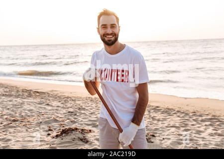 Lächelnden jungen Mann freiwillige Reinigung Strand Müll aus Stockfoto