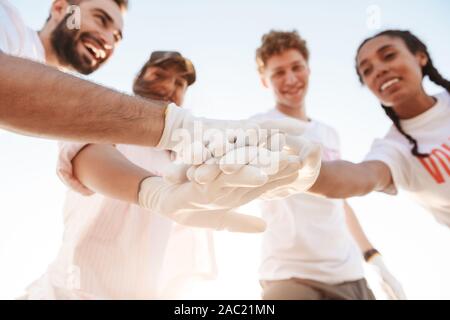 Gruppe von jungen Fröhlichen Freunden freiwillige Reinigung Strand von Müll, die hohe fünf Stockfoto