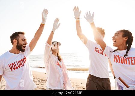 Gruppe von jungen Fröhlichen Freunden freiwillige Reinigung Strand von Müll, die hohe fünf Stockfoto