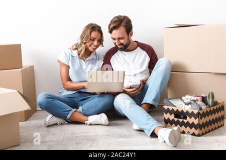 Glückliches Paar schöne Umzug in eine neue Wohnung, sitzen auf einer Etage mit Kästchen umgeben, mit Laptop Stockfoto